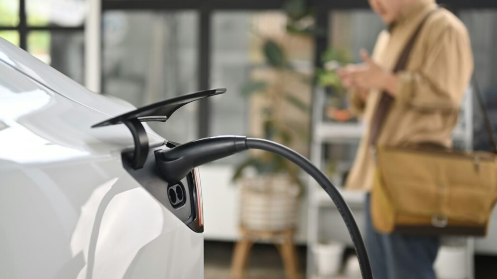 Electric car plugged in to charge outside home with young businessman standing in background